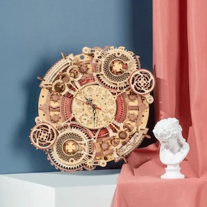 May include: A wooden clock with a complex gear design, featuring a light brown and reddish-brown color scheme. The clock has a round face with Roman numerals and intricate details. The clock is displayed on a white surface against a blue background.
