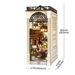 Op de afbeelding: Een gedetailleerd houten model van een Parijs caf&eacute;, met een smeedijzeren balkon, straatlantaarns en een kleine tafelsetting. Het model is 25,5 cm hoog, 19,5 cm breed en 10,6 cm diep. De tekst "Paris" en "Arcade Dating" zijn zichtbaar. Een charmant decoratief item.