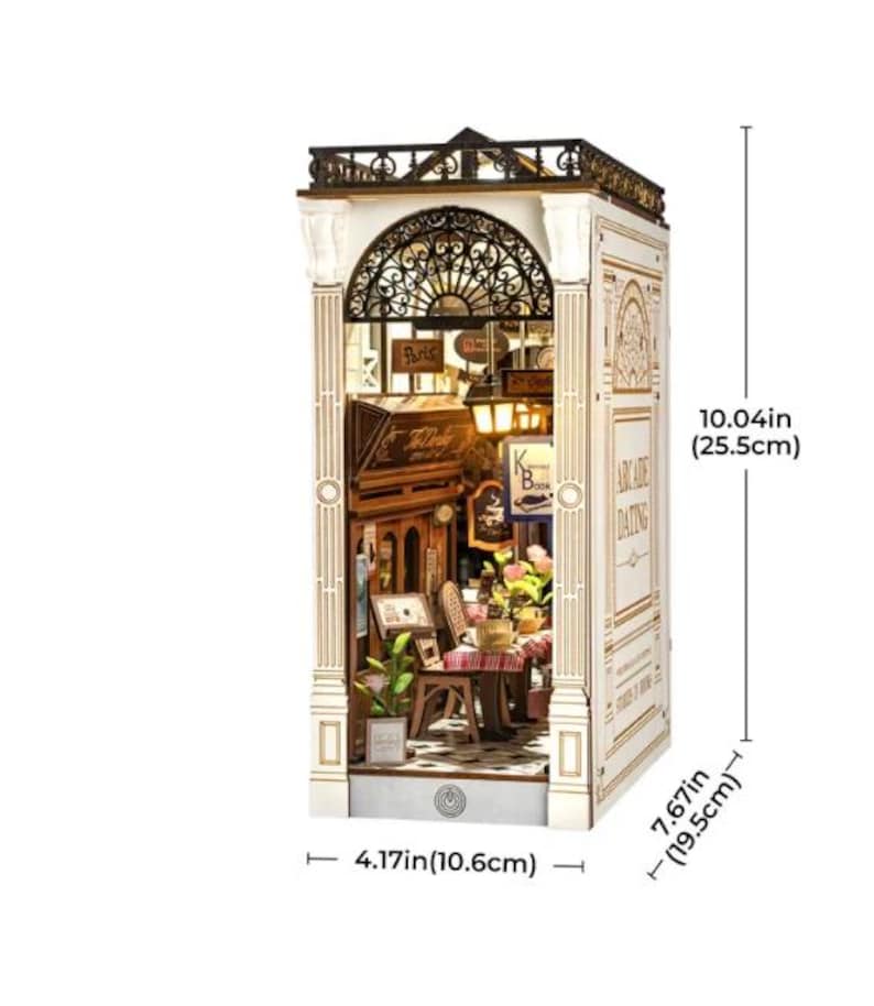 Op de afbeelding: Een gedetailleerd houten model van een Parijs caf&eacute;, met een smeedijzeren balkon, straatlantaarns en een kleine tafelsetting. Het model is 25,5 cm hoog, 19,5 cm breed en 10,6 cm diep. De tekst "Paris" en "Arcade Dating" zijn zichtbaar. Een charmant decoratief item.