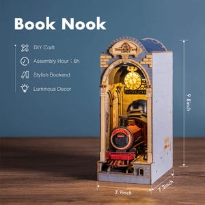 Op de afbeelding: Een houten "Book Nook" model met een treinstation ontwerp en een trein binnenin. Het model is 24,9 cm hoog, 18,3 cm breed en 9,9 cm diep. Het heeft een klok en lichtgevende decoratie. De tekst op het model luidt "Time Travel".