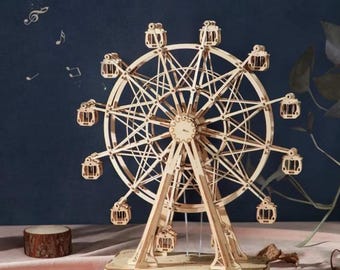 May include: A wooden Ferris wheel model with intricate details, featuring small cabins and a complex spoke design. The text "Music: Around The World In 80 Days" is at the top. The model is set against a dark blue background.