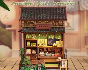 Puede incluir: Maqueta en miniatura de una tienda japonesa de madera, con tejado de tejas, detalles de bambú y detalles verdes. El modelo incluye estanterías con objetos en miniatura, un pequeño letrero y el texto "Kanmi-dokoro Kurihara Assemble / Gift / Decoration".