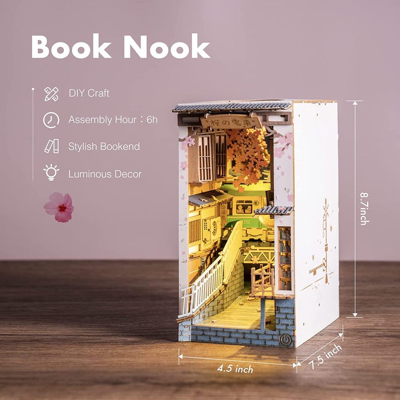 Op de afbeelding: Een DIY Book Nook, een stijlvolle boekensteun met lichtgevende decoratie. De miniatuursc&egrave;ne toont een Japanse straat met gebouwen, een brug en kersenbloesems. Het meet 22 cm hoog, 19 cm breed en 11 cm diep.
