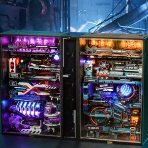 May include: Two illuminated display cases with a futuristic theme. The left case has purple lighting, the right orange. Both feature detailed miniature components, signs, and text, creating a complex, layered design. The cases are black with clear front panels. The design is intricate.