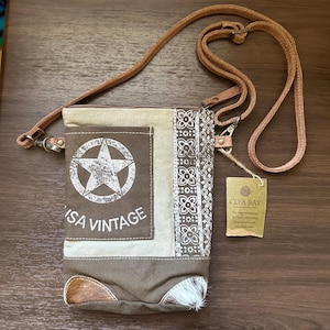 May include: A brown and tan crossbody bag with a leather strap. The bag features a star graphic and the words "ISA VINTAGE". The bag has a decorative pattern on the side and a small tag that says "CLEA RAY".