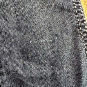 May include: Close-up of dark blue denim fabric with a subtle diagonal weave pattern. The fabric has a slightly worn look with a few faint white marks.