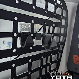 May include: Black metal cargo organizer with two black plastic hooks attached. The organizer has a grid pattern and is mounted in a vehicle. The text "YOTA TWINS" is visible in the lower right corner.