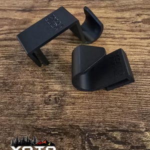 May include: Two black plastic hooks with the text "YOTA TWINS" printed on them. The hooks are on a wooden surface. The text "MIXED HOOKS" is printed below the hooks.