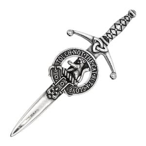 May include: A silver kilt pin featuring a sword with a Celtic knot design and a circular crest with the text "Touch not the cat but a glove".