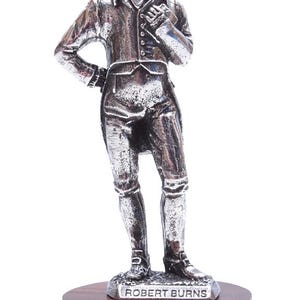 May include: A silver pewter figurine of Robert Burns, the Scottish poet, standing on a wooden base. The base is inscribed with "Robert Burns" and "St Kilda".