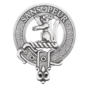 May include: A silver-toned pewter clan crest featuring a rampant lion with a crown on its head, surrounded by a circle with the text "SANS PEUR" in a decorative font. The crest is attached to a decorative base with a fleur-de-lis design.