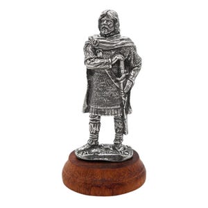 Peut inclure: Une figurine en étain argenté d'un guerrier debout sur une base en bois. Le guerrier porte une armure de mailles et une cape, et tient une épée dans sa main droite.