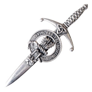 Peut inclure: Une épingle de kilt argentée représentant un motif d'épée avec un nœud celtique et une crête circulaire avec le texte "Vincere Vel Mori".