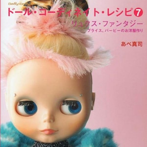 以下が含まれることがあります： ピンクの羽根で飾られたブロンドの髪をまとめたお団子ヘア、青い瞳、青いファーコートを着た人形。人形は黒いキラキラのドレスにピンクのベルトをしています。背景はピンクです。