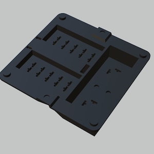 May include: Black plastic mold with multiple rectangular and circular cutouts. The mold is designed for creating small objects.