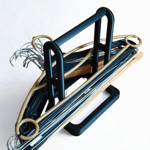 Peut inclure: Un organisateur de cintres en métal noir rempli de cintres variés. Les cintres sont un mélange de noir, beige et fil d'argent. L'organisateur a une poignée et une base rectangulaire.