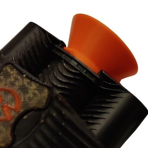 Könnte beinhalten: Ein Gerät in Schwarz und Tarnmuster mit einer orangefarbenen Gummiplatte und zwei zusätzlichen Spitzen, eine weiße und eine schwarze.