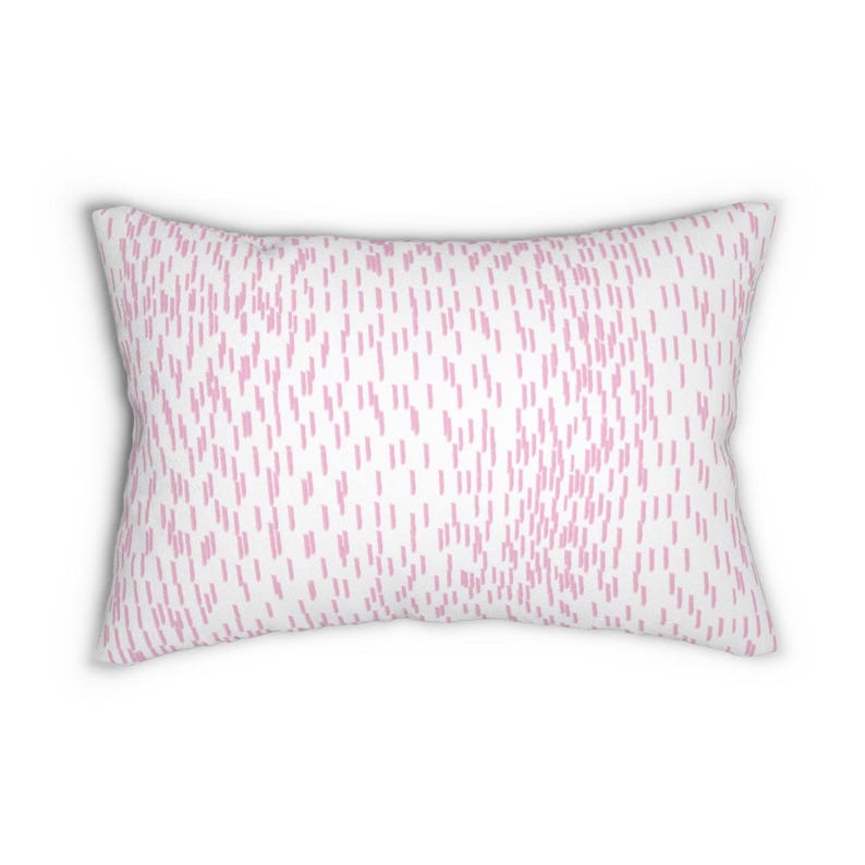 May include: A rectangular throw pillow featuring a white background with a repeating pattern of small, vertical, light pink dashed lines distributed across the entire surface of the fabric, creating a consistent and uniform textured appearance.