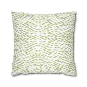 May include: A square throw pillow featuring a white background with a repeating pattern of small, light green, oval-shaped dots. The dots are arranged in a symmetrical, diamond-like formation that spans across the entire surface of the pillow.