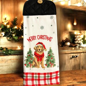 Puede incluir: Un paño de cocina con temática navideña con una parte superior acolchada negra y un cierre de botón. El paño blanco presenta un diseño festivo con un golden retriever con gorro y bufanda de Papá Noel, las palabras "Merry Christmas", copos de nieve y árboles de Navidad.
