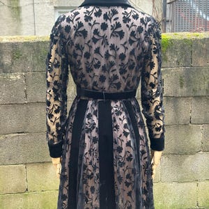 May include: A black vintage dress with a floral lace overlay. The dress features a velvet collar, a matching belt, and long sleeves. The skirt has vertical velvet panels alternating with the lace.