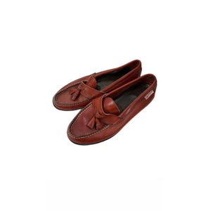 May include: A pair of brown leather loafers with tassel details. The shoes have a classic design with visible stitching and a rounded toe. The loafers are a reddish-brown color.