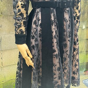 May include: A black dress with a velvet bodice and skirt panels, accented with sheer floral lace. The dress features long sleeves with velvet cuffs and a matching belt. The dress is displayed on a mannequin.