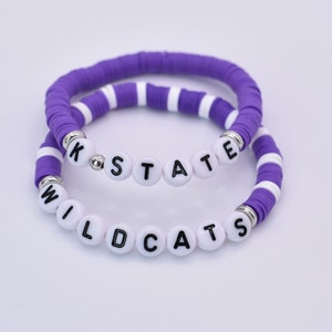 May include: Two purple and white beaded bracelets with the words "K-STATE" and "WILDCATS" spelled out in white beads.