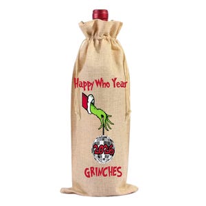 May include: A burlap wine bottle bag with a red bottle top. The bag features the text "Happy Who Year" and "2026 GRINCHES" in red. A green hand and a disco ball are also on the bag.