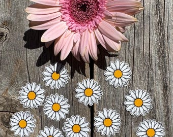 May include: A pink gerbera daisy with a yellow center is surrounded by 15 white daisy stickers with yellow centers on a wooden background.