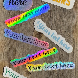 May include: Assortment of customizable holographic stickers with the text "Your text here" in various fonts and colors. The stickers are on a wooden background. The text "40 Fonts 36 Colors" is also visible on one of the stickers.