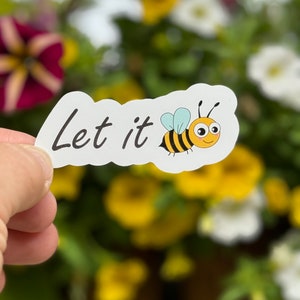 May include: White sticker with the text "Let it" and a cartoon bee with black and yellow stripes and a smiling face.
