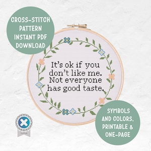 Puede incluir: Un patrón de punto de cruz en un aro de madera con la frase "It's ok if you don't like me. Not everyone has good taste." El diseño incluye una corona floral con flores azules y melocotón. Texto adicional en la imagen dice "Descarga instantánea de PDF del patrón de punto de cruz."
