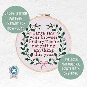 May include: A cross-stitch pattern in a wooden hoop. The text reads "Santa saw your browser history. You're not getting anything this year." The design includes a green wreath with red berries and a red bow.