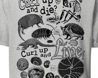 May include: A gray t-shirt with a black and white graphic design. The graphic features a variety of animals, including armadillos, a hedgehog, and a pill bug. The text on the shirt reads "Curl up and die? No. Curl up and Live!"
