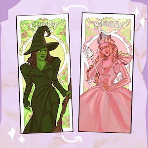 May include: Two art prints featuring characters from the musical "Wicked." One print shows a green-skinned woman in a black witch's hat and dress, labeled "Elphaba." The other depicts a woman in a pink dress and crown, labeled "Glinda."