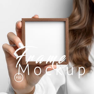 May include: A square, brown wooden frame with a white interior is held up. The frame has the text "Frame Mockup" in white script across the front. The image also includes the text "Gift for You" and "I Mock-Up Free".