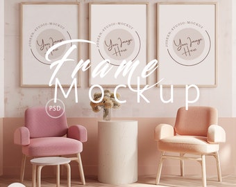 May include: Three framed pictures with a light brown frame hanging on a light pink wall. The frames are empty and have the text "JOBERN-STUDIO-MOCKUP" and "Your Image Here" in a circle. Two pink armchairs with wooden legs and a small round table are in front of the wall. A vase with dried flowers is on a round concrete table.