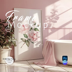 May include: A white frame mockup with a floral print of pink roses on a white background. The frame is leaning against a pink wall in a bathroom setting. A white bathtub with a pink towel draped over the side is in the foreground. The text "Frame Mockup" is written in white on the frame.