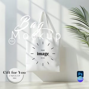 May include: White tote bag mockup with the text "YOUR image HERE" in a circle. The bag is hanging on a white wall with a plant in the background.