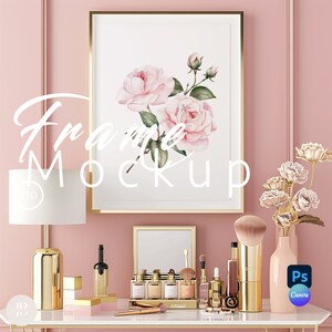 May include: A gold framed picture with a watercolour painting of pink roses on a white background. The picture is hanging on a pink wall above a white table with a gold lamp, a vase of flowers, and a variety of makeup and beauty products.