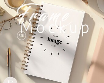May include: A white spiral bound notebook with the text "Frame Mockup" written in black cursive. The notebook has a black and white graphic of a clock with the text "Your image here" inside the clock.