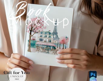May include: A white book mockup with a watercolor illustration of a Parisian cafe with the Eiffel Tower in the background. The text "Book Mockup" is written in a handwritten font above the illustration. The text "Gift for You" is written in a circle below the book.