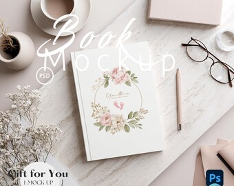 May include: A white book mockup with a floral design, a cup of coffee, glasses, and a pencil. The book cover features a gold wreath with pink flowers and the text "Chu Atman". The image also includes the text "Book Mockup", "Gift for You", and "1 Mock-up Free".