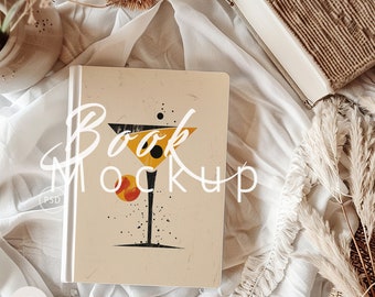 May include: A book mockup with a white background and a design of a yellow and black cocktail glass with a red and orange circle on the front. The text "Book Mockup" is written in white on the front of the book.