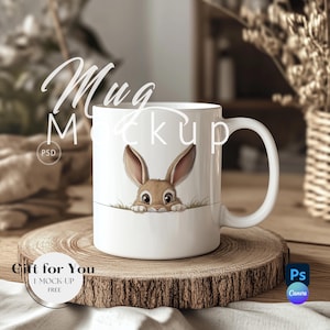 Puede incluir: Taza de cerámica blanca con un conejito marrón asomándose por el borde. La taza está sobre un posavasos de madera y una superficie de tela blanca.