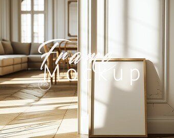 May include: A gold frame mockup in a white room with a couch and a window in the background. The frame is sitting on a wooden floor.