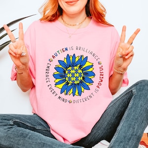 May include: Pink t-shirt with a colorful sunflower design and the text "Autism is brilliance, embrace every mind, different is powerful".