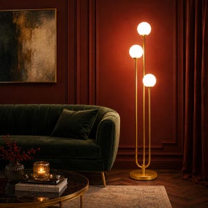 May include: A tall floor lamp featuring a gold-toned metal stand with three vertical rods of varying heights, each topped with a spherical white glass globe light. The lamp has a circular base and emits a warm, soft glow from the three illuminated bulbs.