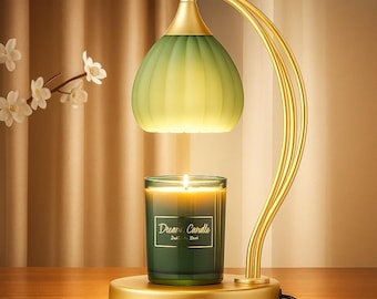 May include: A gold-colored candle warmer with a green glass shade and a base. A lit candle in a green glass jar sits on the base. The candle jar has the text "Dream Candle". The warmer has a curved design.